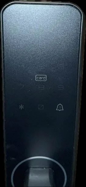 Ein elegantes digitales Türschlosspanel mit schwarzer Oberfläche. Es verfügt über einen Ziffernblock mit den Ziffern 0–9. Es gibt Symbole für Schlüsselkarte, Sternchen, Null und Türklingel. An der Unterseite befindet sich ein gebogener Griff zum Ver- und Entriegeln der Tür.